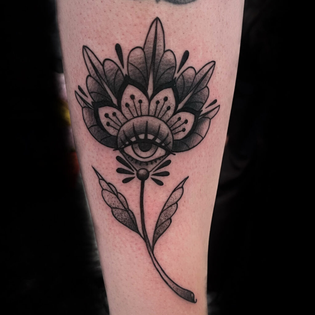 Tatouage style traditionnel en noir et gris d'une fleur ornementale avec un oeil