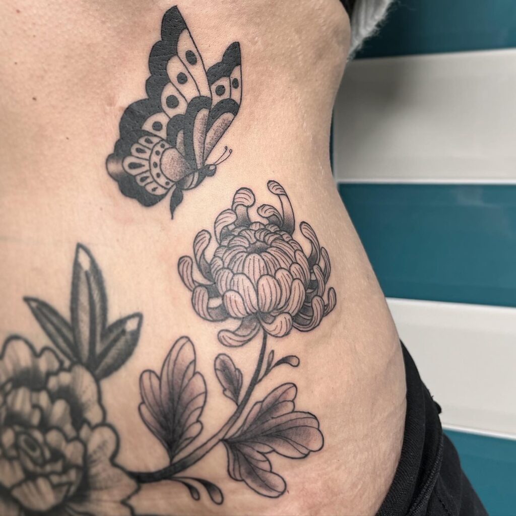 Tatouage style traditionnel en noir et gris d'un papillon au dessus d'un chrysanthème japonais